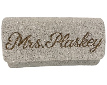 May include: A white beaded clutch with the text "Mrs. Plaskey" embroidered in gold.