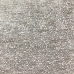 May include: Close-up of a textured, light gray fabric. The material has a subtle, dotted pattern and a slightly uneven surface, creating a soft, tactile appearance. The fabric appears to be a knit or woven textile, suitable for clothing or home decor.