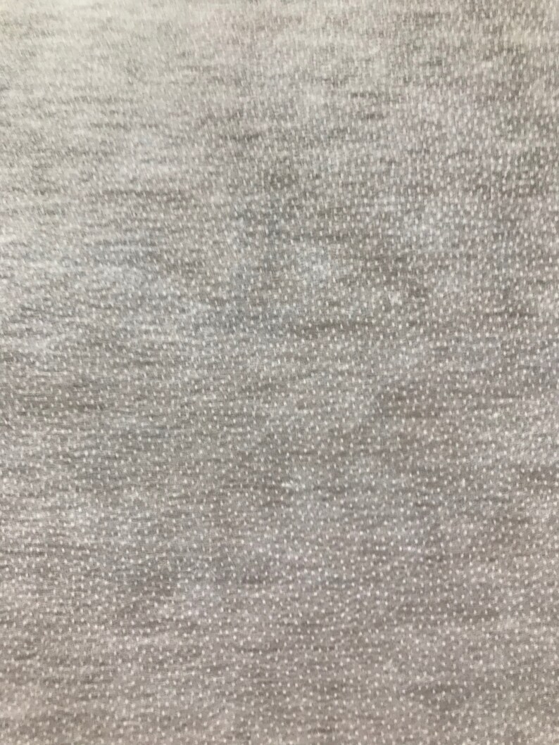 May include: Close-up of a textured, light gray fabric. The material has a subtle, dotted pattern and a slightly uneven surface, creating a soft, tactile appearance. The fabric appears to be a knit or woven textile, suitable for clothing or home decor.