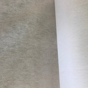 May include: A close-up view of two rolls of fabric. One roll is a light beige color with a textured surface. The other roll is white and appears to be a smooth, plain fabric. The fabrics are side by side.