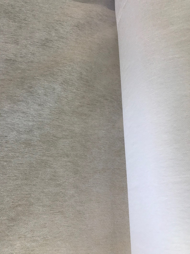May include: A close-up view of two rolls of fabric. One roll is a light beige color with a textured surface. The other roll is white and appears to be a smooth, plain fabric. The fabrics are side by side.