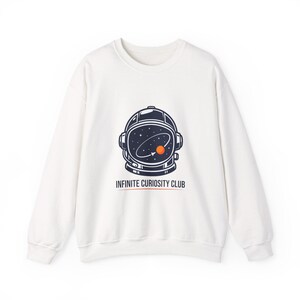 May include: White crew neck sweatshirt featuring a navy blue astronaut helmet graphic. The helmet design includes a starry sky and an orange planet. The text "INFINITE CURIOSITY CLUB" is printed below the graphic in navy and orange.