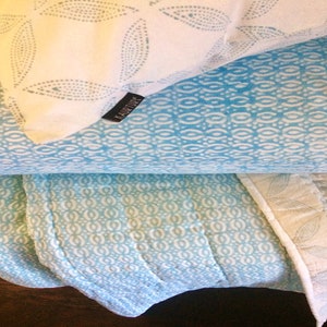 May include: A stack of three blue and white patterned throw pillows with a white pillow on top featuring the word "HABITUDE" in black text.