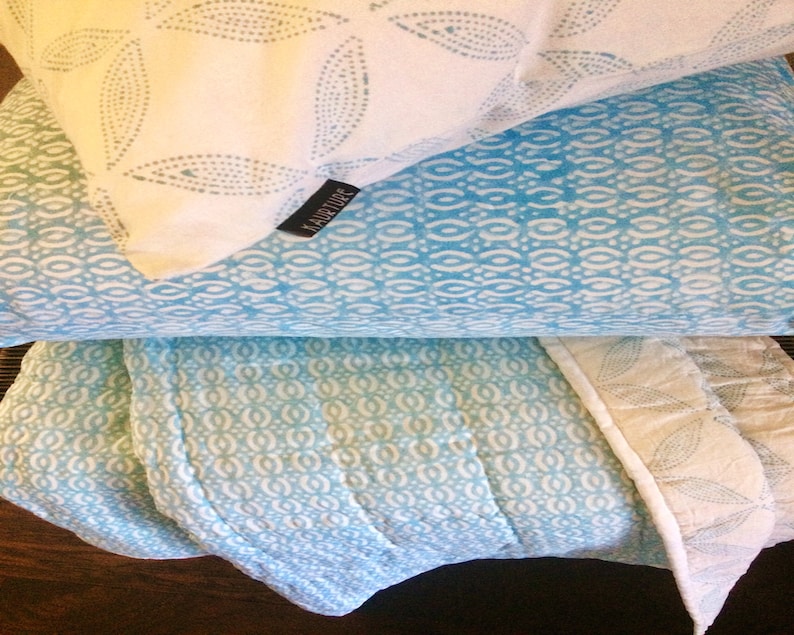 May include: A stack of three blue and white patterned throw pillows with a white pillow on top featuring the word "HABITUDE" in black text.