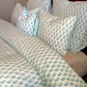 May include: A white duvet cover and pillowcases with a teal floral pattern. The bedding is arranged on a bed with a wooden headboard.