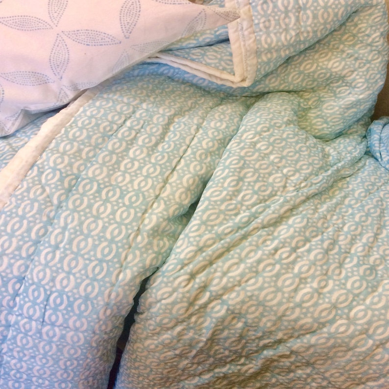 May include: A blue and white patterned quilt with a white border. The quilt is made of a soft, lightweight fabric and has a subtle sheen.
