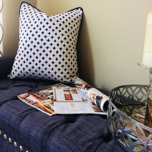 May include: A navy blue and white patterned throw pillow sits on a dark blue tufted bench with a magazine and a silver decorative tray on top.
