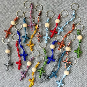 May include: A collection of colourful knotted keychain crosses with wooden beads. The keychains are made with different coloured cords and feature a variety of cross designs.