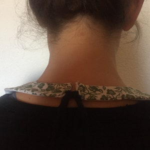 Peut inclure: Un chemisier noir avec un col floral blanc et vert. Le col est nou&eacute; &agrave; l'arri&egrave;re avec une ficelle noire.