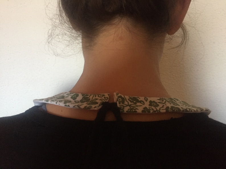 Peut inclure: Un chemisier noir avec un col floral blanc et vert. Le col est nou&eacute; &agrave; l'arri&egrave;re avec une ficelle noire.