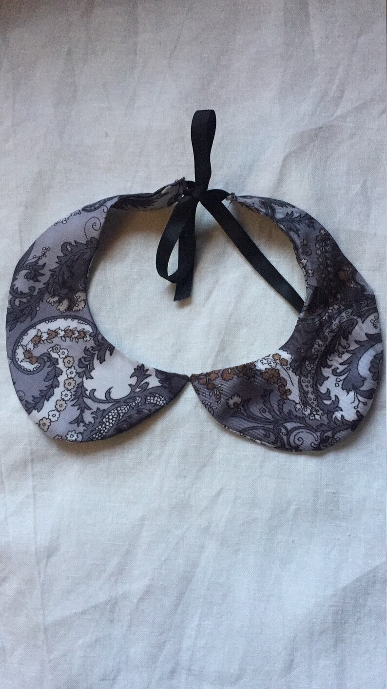 Peut inclure: Un col en tissu &agrave; motif paisley gris et marron avec un ruban noir.
