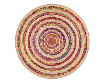 Op de afbeelding: Ronde jute vloerkleed met concentrische cirkels. Het vloerkleed heeft een gevlochten ontwerp met banden in natuurlijk beige en kleurrijke tinten rood, geel, blauw en paars. Geschikt voor binnenshuis, de diameter is ongeveer 150 cm.