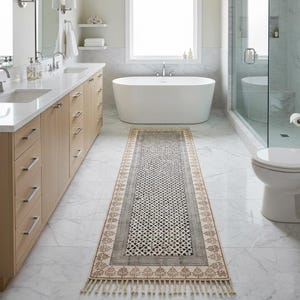 May include: A rectangular bathroom rug with a geometric pattern in black and white, framed by a gray border and a beige border with a tree design. The rug has a fringe on both ends. The rug is placed in a modern bathroom.