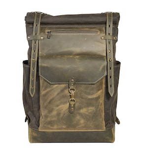 Op de afbeelding: Een bruine leren en canvas rugzak met een groot voorvak en verstelbare banden.