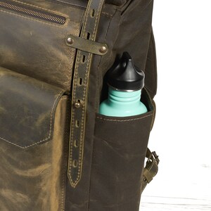 Op de afbeelding: Een groene leren rugzak met een groot voorvak en een zijvak waarin een turquoise waterfles zit.