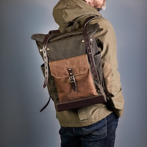 Könnte beinhalten: Ein brauner und grüner Canvas-Rucksack mit Lederriemen und Schnallen. Der Rucksack hat ein großes Hauptfach und eine kleinere Fronttasche.