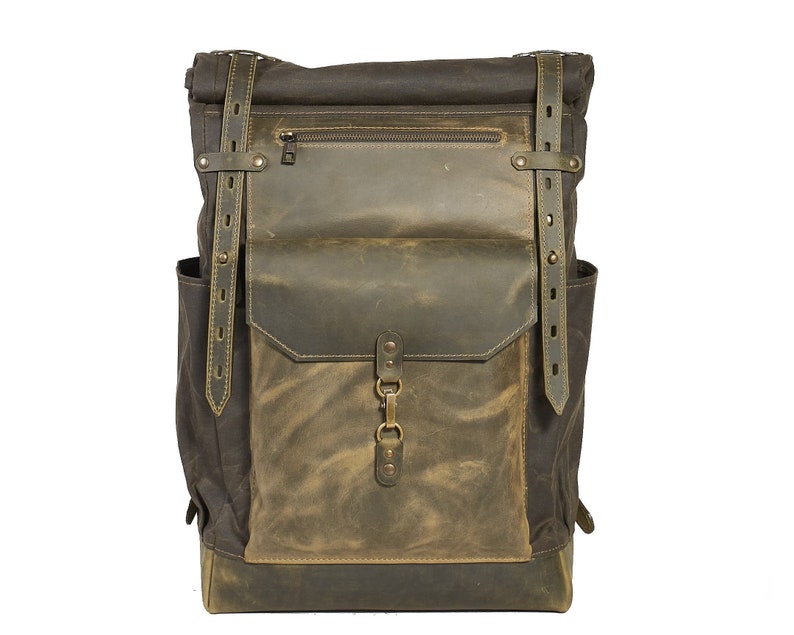 Op de afbeelding: Een bruine leren en canvas rugzak met een groot voorvak en verstelbare banden.
