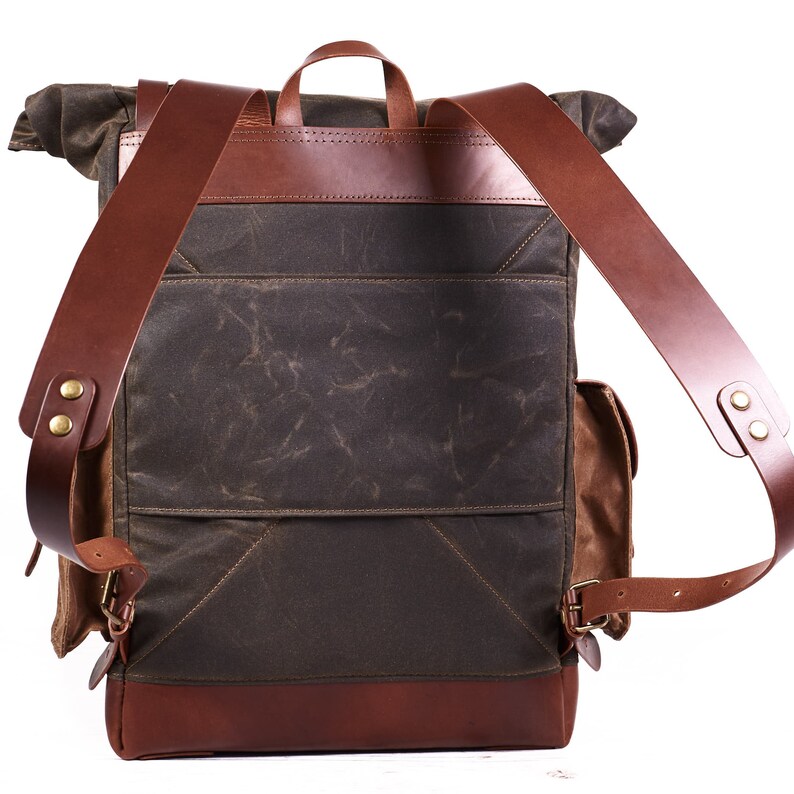 Puede incluir: Una mochila de lona verde y cuero marr&oacute;n con correas ajustables y cierre de solapa. La mochila tiene un compartimento principal grande y un bolsillo frontal m&aacute;s peque&ntilde;o.