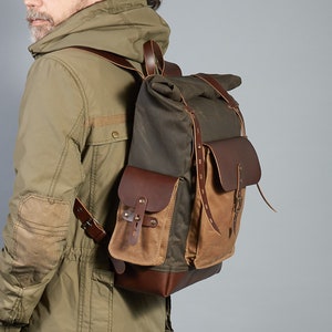 Puede incluir: Una mochila de cuero marr&oacute;n y lona con cierre de rollo. La mochila tiene un compartimento principal grande, un bolsillo frontal y correas ajustables.