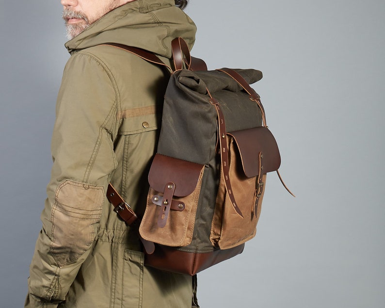 Puede incluir: Una mochila de cuero marr&oacute;n y lona con cierre de rollo. La mochila tiene un compartimento principal grande, un bolsillo frontal y correas ajustables.