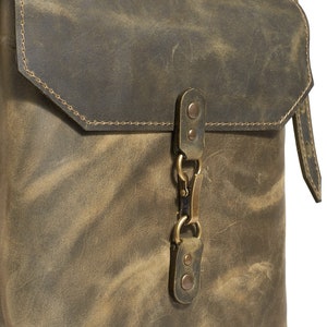 Op de afbeelding: Een bruine leren schoudertas met een klep sluiting en een messing gesp. De tas heeft een verweerde look en is gemaakt van hoogwaardig leer.