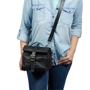 Puede incluir: Bolso mensajero negro con cierre enrollable, correa de cuero y hebilla plateada. El bolso tiene un asa superior y una correa de hombro larga y ajustable. El bolso est&aacute; hecho de un material duradero y resistente al agua.