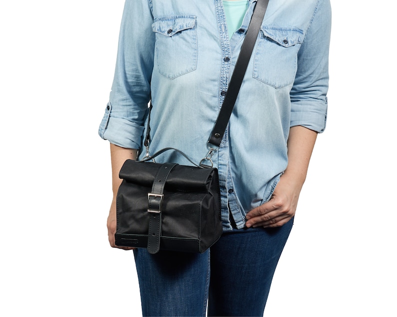 Puede incluir: Bolso mensajero negro con cierre enrollable, correa de cuero y hebilla plateada. El bolso tiene un asa superior y una correa de hombro larga y ajustable. El bolso est&aacute; hecho de un material duradero y resistente al agua.