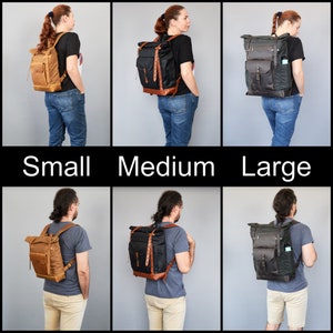 Op de afbeelding: Drie canvas rugzakken in verschillende maten: klein, medium en groot. De rugzakken zijn bruin, zwart en donkergroen. Elke rugzak heeft een roll-top sluiting, leren banden en een voorvak.