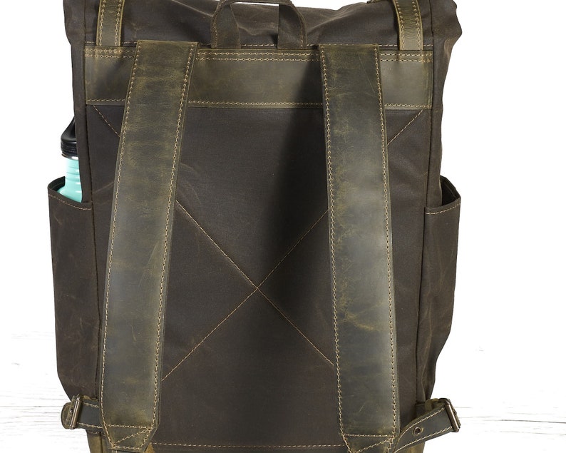 Op de afbeelding: Een bruine leren rugzak met verstelbare schouderbanden. De rugzak heeft een groot hoofdvak en een kleiner vak aan de voorkant.