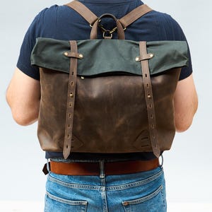 Peut inclure: Un sac à dos en cuir marron avec un rabat en toile verte et des bretelles réglables. Le sac à dos a une fermeture à boucle et des accessoires en laiton.