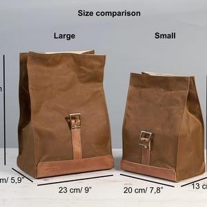 Puede incluir: Dos bolsas de lona encerada marr&oacute;n, etiquetadas como "Large" y "Small", con detalles de cuero y cierres de hebilla. La bolsa grande mide 35 cm de alto, y la peque&ntilde;a 28 cm. Comparaci&oacute;n de tama&ntilde;os.
