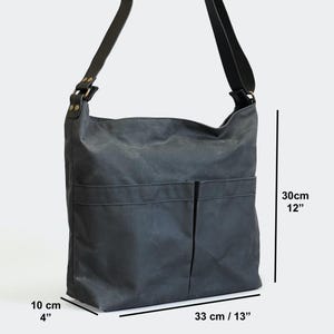 May include: A dark gray shoulder bag with a long strap, two front pockets, and brass-toned rivets. The bag measures 12 inches in height, 13 inches in width, and 4 inches in depth, as indicated by the visible measurement text on the image.
