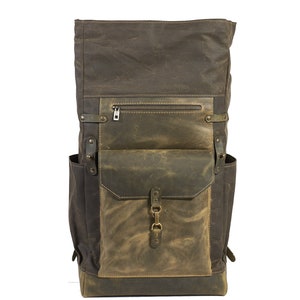 Op de afbeelding: Een bruine en groene canvas en leren rugzak met een groot voorvak en een ritsvak op de bovenklep.