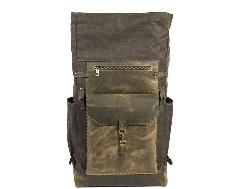 Op de afbeelding: Een bruine en groene canvas en leren rugzak met een groot voorvak en een ritsvak op de bovenklep.
