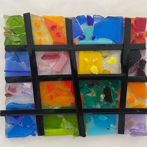 May include: A colorful mosaic artwork with a grid pattern. The artwork is made of small pieces of glass in various colors, including blue, green, yellow, orange, and red. The grid is made of black lines.