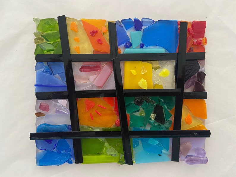 May include: A colorful mosaic artwork with a grid pattern. The artwork is made of small pieces of glass in various colors, including blue, green, yellow, orange, and red. The grid is made of black lines.