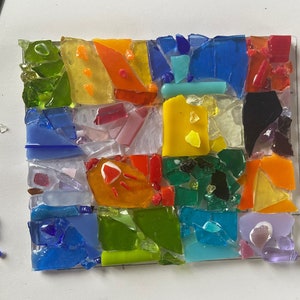 May include: A colorful mosaic artwork made of small pieces of glass in various shades of red, orange, yellow, green, blue, and purple. The mosaic is arranged in a grid pattern, creating a geometric design.