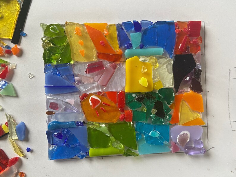 May include: A colorful mosaic artwork made of small pieces of glass in various shades of red, orange, yellow, green, blue, and purple. The mosaic is arranged in a grid pattern, creating a geometric design.