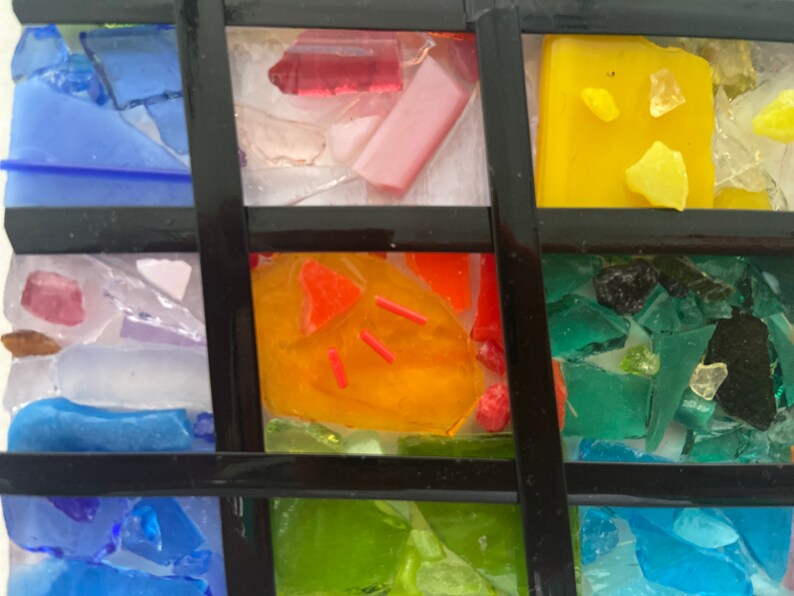 May include: A mosaic artwork made of small pieces of glass in various colors, including blue, green, yellow, orange, and pink. The glass pieces are arranged in a grid pattern, creating a geometric design.