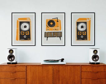 May include: Three framed wall art prints featuring graphic illustrations of audio equipment in orange, black, and white. Two prints depict speakers, while the center print shows a turntable on a stand. The art is displayed above a wooden sideboard.