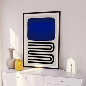 May include: A framed wall art print featuring a large solid dark blue rectangle positioned above a series of three stacked black horizontal U-shaped lines, all set against a light gray background within a thin black frame.