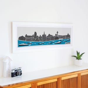 Puede incluir: Una ilustraci&oacute;n en blanco y negro enmarcada del horizonte de Liverpool con el texto "LIVERPOOL" en la esquina inferior derecha. La ilustraci&oacute;n representa los edificios de la ciudad y el r&iacute;o Mersey con barcos.