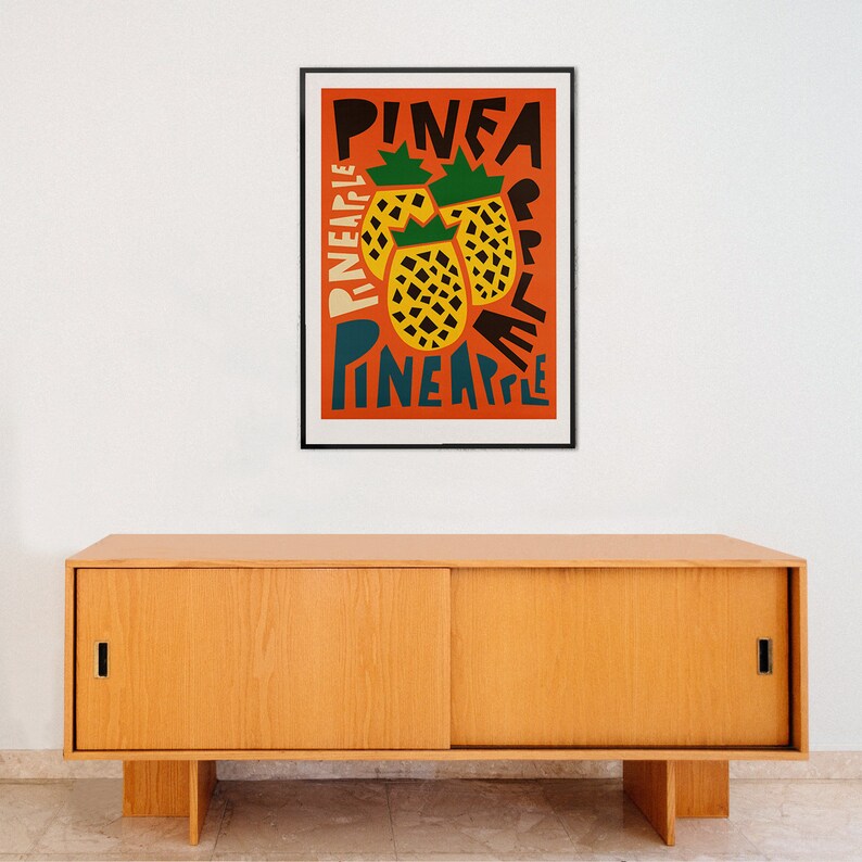 May include: A framed poster with a red background and a stylized illustration of pineapples. The text "PINEA PINEAPPLE" is written in black and blue letters.