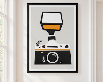 May include: A framed graphic art print featuring a stylized camera with a large flash attachment. The camera is black, white, and orange, set against a light gray background. The design uses bold, geometric shapes to depict the camera body and flash.