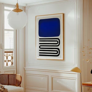 May include: A rectangular wall art print in a gold frame featuring a solid dark blue rounded rectangle shape positioned above a series of three stacked black horizontal U-shaped lines on a light beige background, displayed on a white wall.