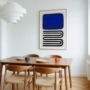 May include: A framed wall art print featuring a solid dark blue rectangle positioned above a series of black horizontal U-shaped lines on a light gray background, displayed in a dining room with a wooden table and chairs.
