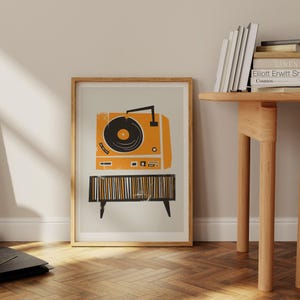 Puede incluir: Una impresi&oacute;n enmarcada de un tocadiscos vintage con un disco negro en un plato giratorio. El tocadiscos es naranja y negro con una base a rayas. La impresi&oacute;n est&aacute; sobre un fondo gris claro.