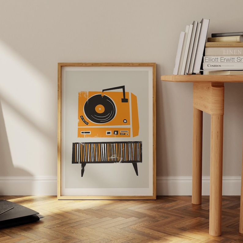Puede incluir: Una impresi&oacute;n enmarcada de un tocadiscos vintage con un disco negro en un plato giratorio. El tocadiscos es naranja y negro con una base a rayas. La impresi&oacute;n est&aacute; sobre un fondo gris claro.