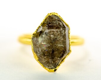 May include: A gold ring with a large, faceted, smoky quartz gemstone. The gemstone is set in a gold bezel and has a rough, natural look.