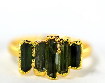 May include: A gold ring featuring a cluster of dark green tourmaline crystals. The crystals are set in a gold bezel setting, creating a striking contrast. The ring is a unique piece of jewelry.
